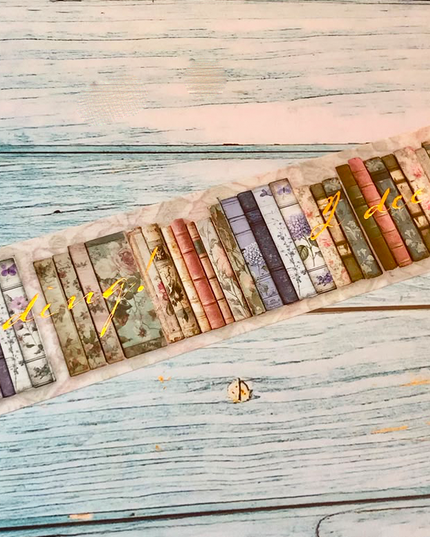 A roll of decorative washi tape featuring a vintage book spine pattern, partially unrolled on a rustic, light blue-gray wooden surface.