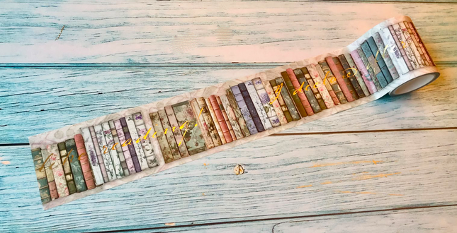 A roll of decorative washi tape featuring a vintage book spine pattern, partially unrolled on a rustic, light blue-gray wooden surface.