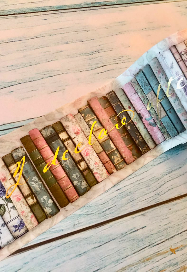 A set of vintage-style book spines themed washi tape set against  a distressed light wood surface. The books feature various patterns and colors including floral, striped, and solid designs in muted tones of pink, blue, green, brown, and beige, with a gold cursive watermark overlay.